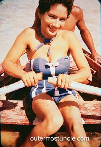 A mysterious and lovely woman in a 1950's bathing suit, rowing a boat. She's looking seductively at the camera.
