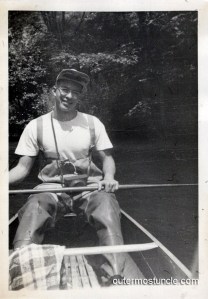 A black and white photo from the 1940's, showing my Uncle Bill in a canoe, wearing hip waders. He has an Argus A2b camera hanging from a strap around his neck. He's smiling for the camera!