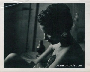 1950's black and white photo of a mysterious woman. She's black and wearing a cocktail dress.