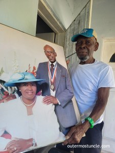 Clifford Fernander a.k.a. Snake Eyes in Cockburn Town, San Salvador Island, Bahamas. He stands on his front porch, holding a portrait of him and his wife.