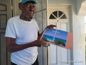 Clifford Fernander a.k.a. Snake Eyes. Here, he's holding a photograph of the Christopher Columbus Monument at Long Bay, San Salvador Island, Bahamas.