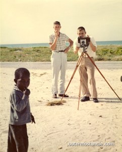 Two white men using a Speedgraphic camera to photograph a young boy in the Bahamas. circa 1957.