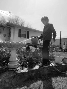 An 88 year old woman, Jamie, hosing her plants while balancing on a brick wall. 