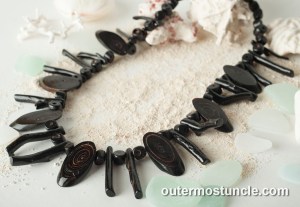 A vintage black coral necklace, arranged on white sand and other beach finds from the Bahamas out islands.