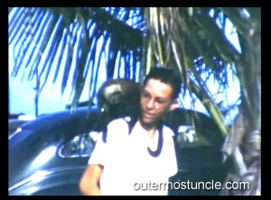 A boy with a monkey on his shoulder in front of palm trees.
