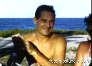 A man, shirtless, at a picnic table.