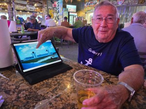 Lou, in his 90's. He's pointing to a photo on his laptop screen. The rest of the bar is in the background.
