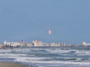 A rocket launches into a clear blue sky, above Cocoa Beach, Florida.