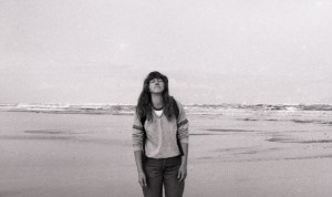 A sepia photograph of me, at 22, head tilted up, eyes closed, standing on an ocean beach.
