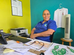 A portrait of Angela, seated, at Riding Rock's front desk, paperwork is arrayed before her.
