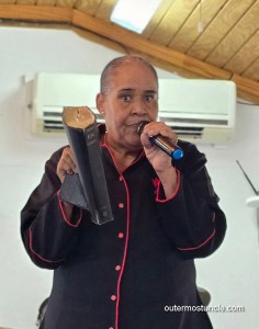 A woman, dressed in a pastor's robe, holding a Bible, while speaking in front of her congregation.