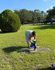 Angela, bent over a grave in a cemetery - placing flowers.