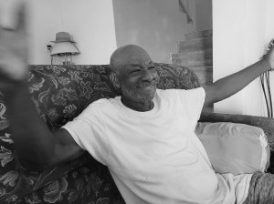 A man sits on his sofa, arms outspread, smiling.