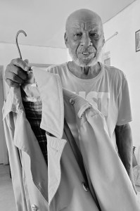 Leon stands in his living room, holding a trench coat on a hanger.